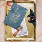 Stylish wedding invitation display with calligraphy and vintage accents on gold tray.