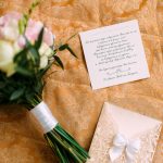 A flat lay of a bridal bouquet and wedding invitation on floral fabric, ideal for wedding themes.